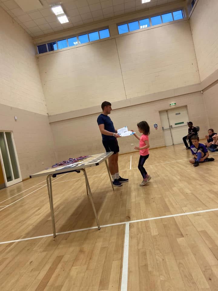 Coach handing a certificate to a child at a sports hall party